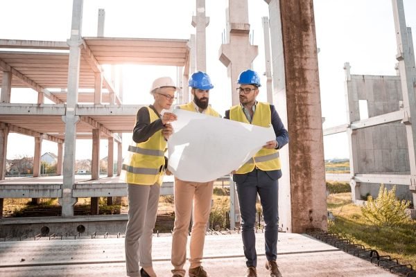 Three architects discussing building plans on a sunny day at a construction site.