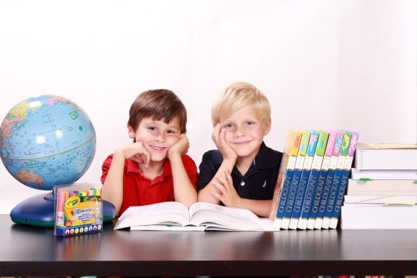 Two boys sitting and smiling at a classroom table studying with books and a globe.