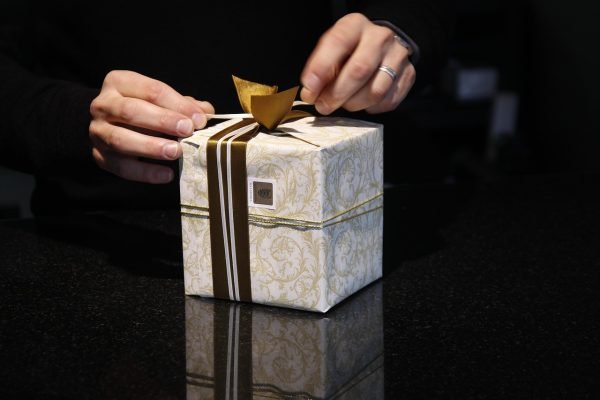 A person is packaging a gift box with a bow.